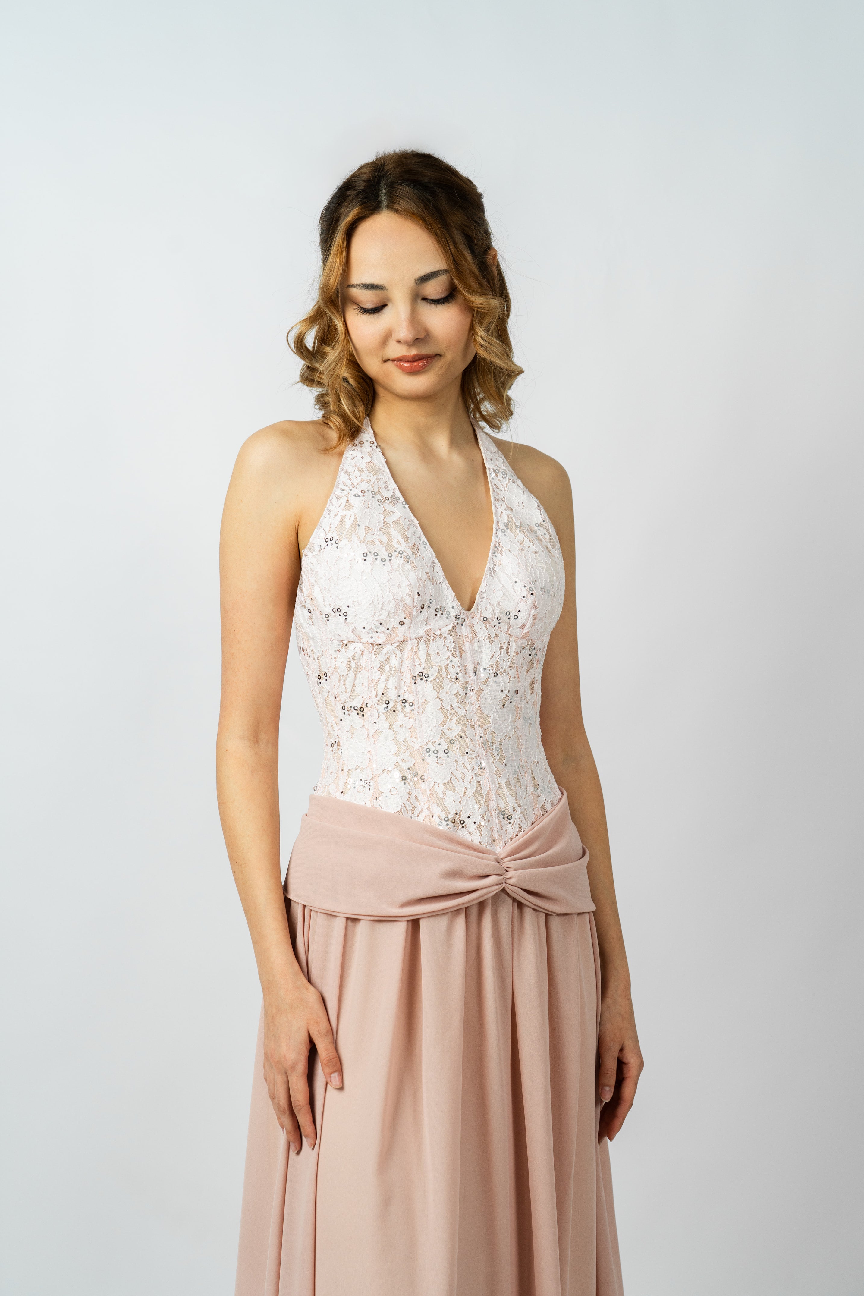 Woman wearing a white lace top and pink skirt on a light gray background