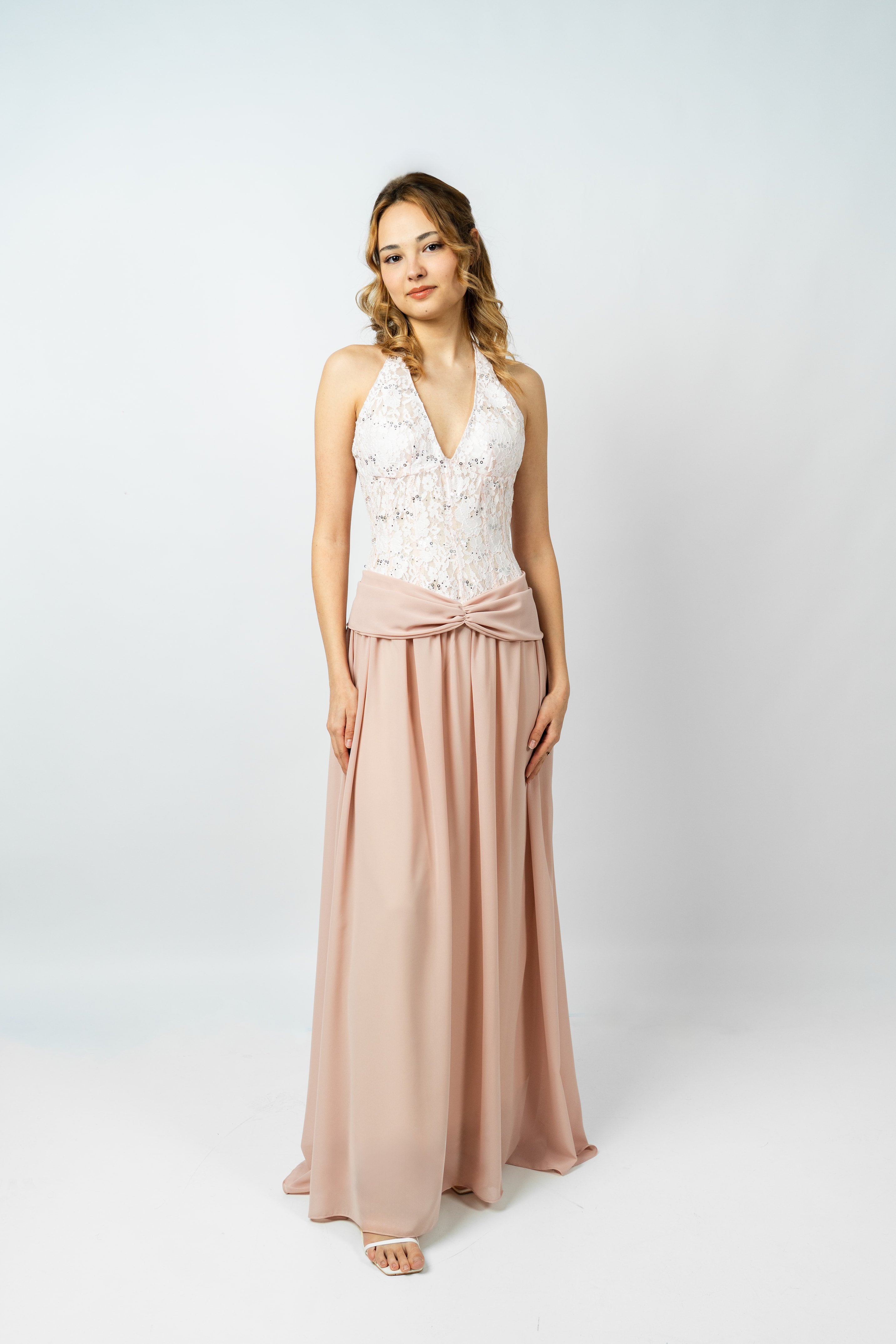 Woman wearing a white lace top and blush pink skirt on a white background