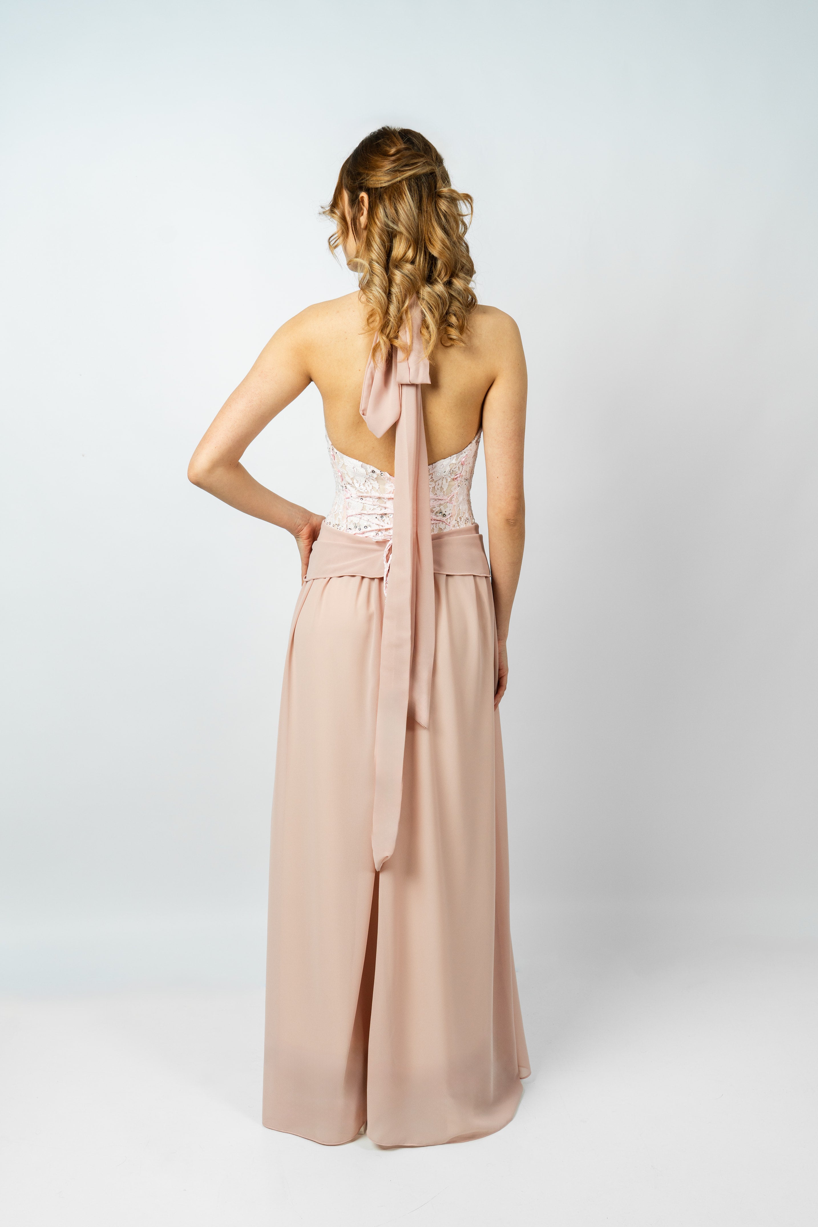 Woman wearing a blush pink jumpsuit with a white lace top on a white background