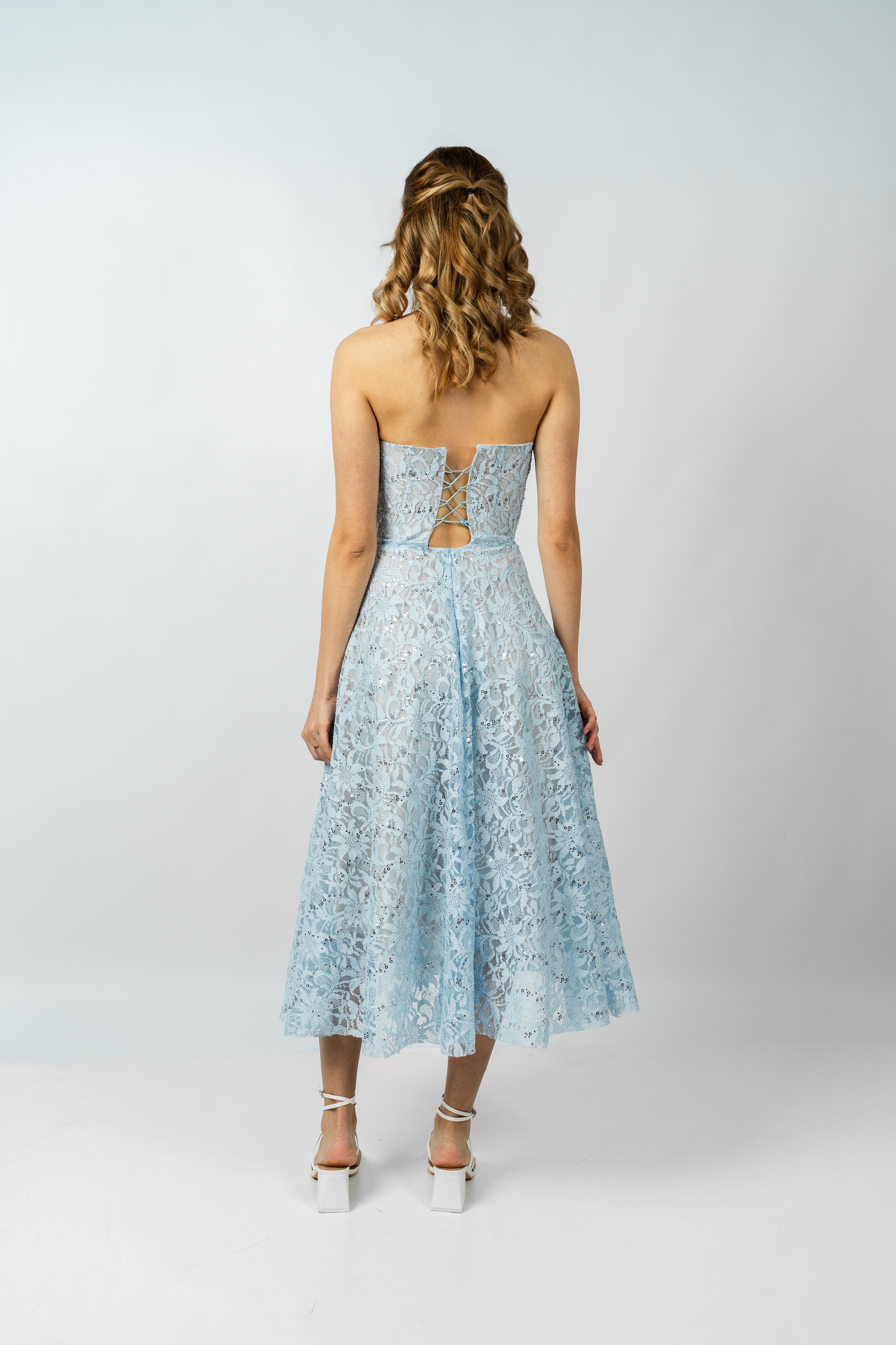 Woman wearing a light blue strapless dress with lace details on a white background