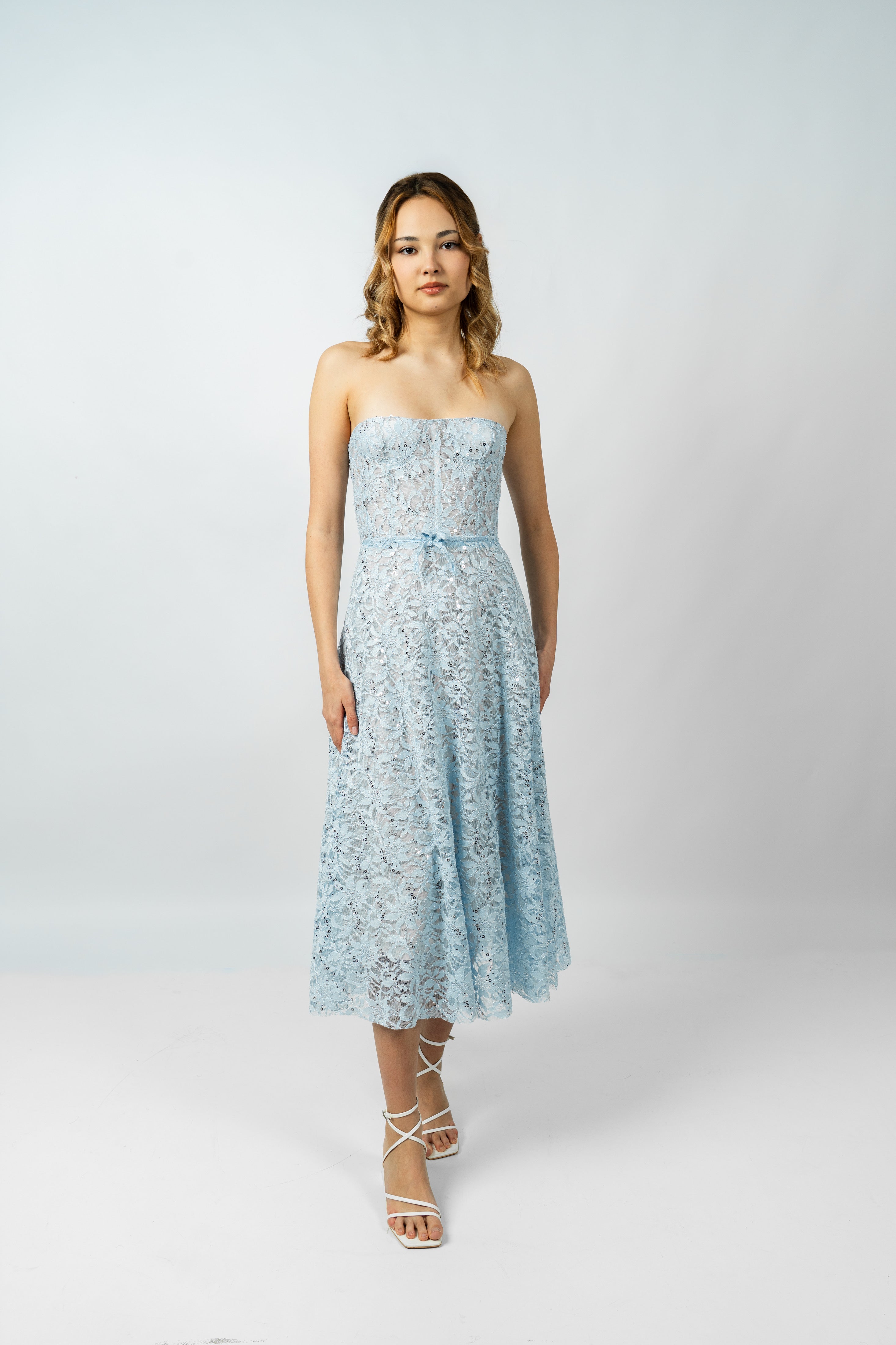 Woman wearing a light blue strapless dress with lace details on a white background