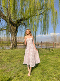 Woman in a strapless floral dress standing under a willow tree by a lake.