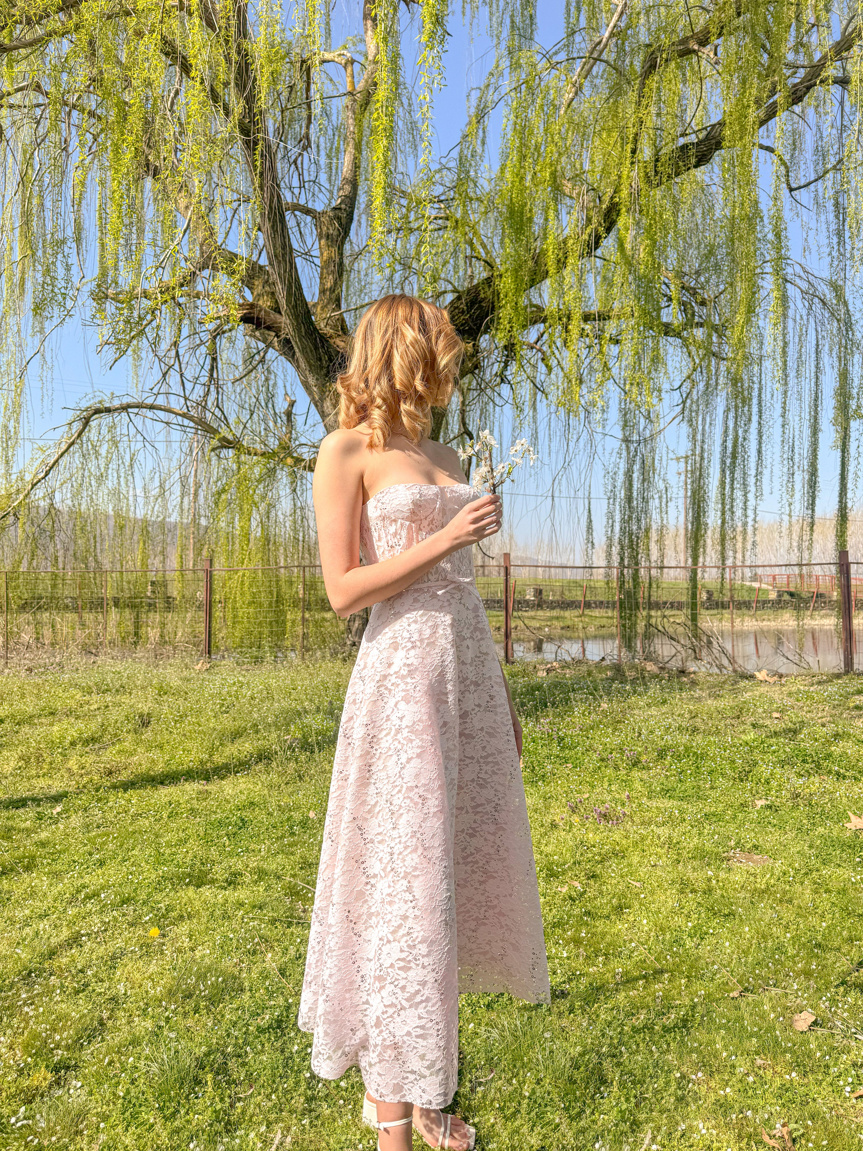 Woman in a white dress standing under a willow tree in a park.